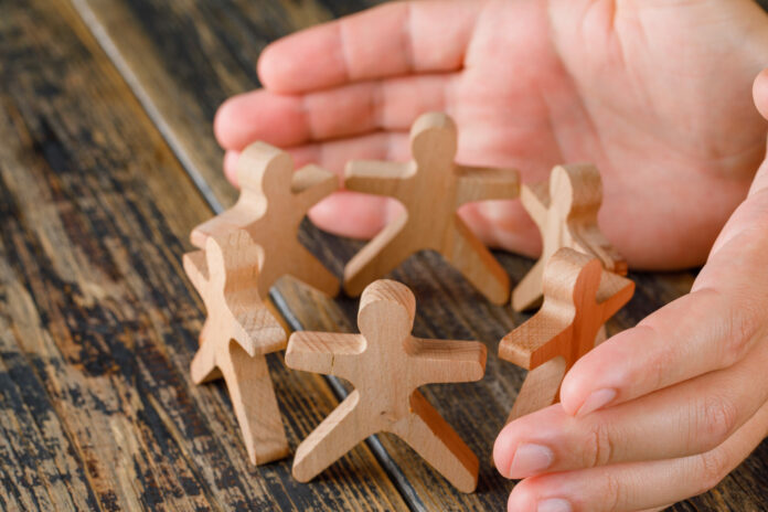 Business success concept on wooden background high angle view hands protecting wooden figures of people